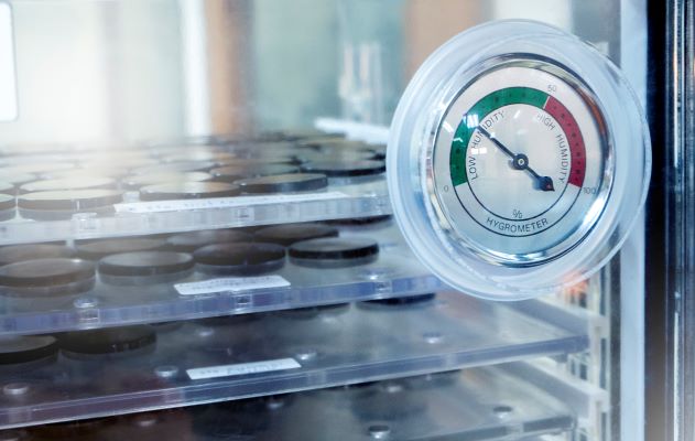 Close-up of a circular dial hygrometer mounted inside an incubator or storage chamber.