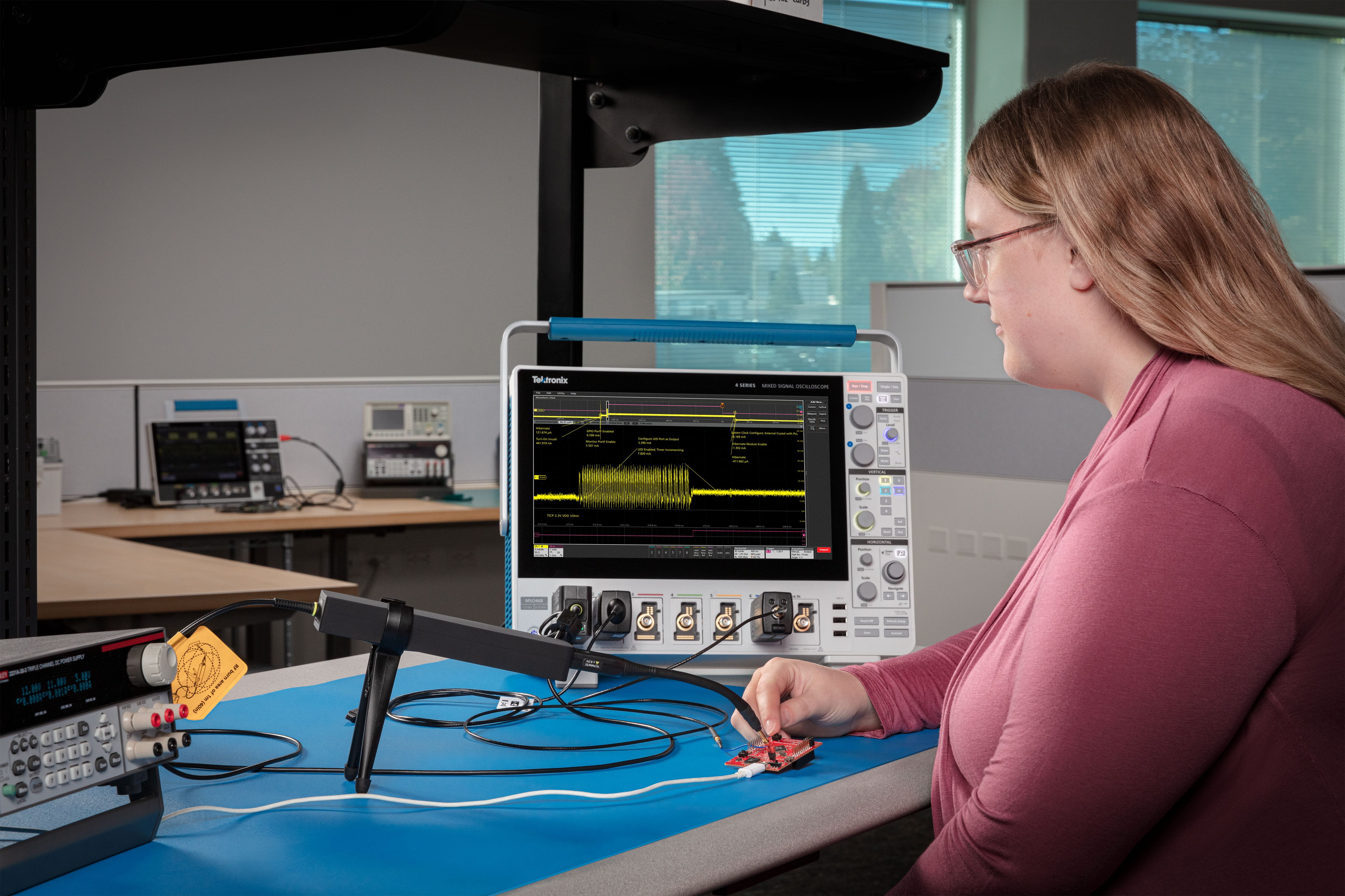 Woman using a Tektronix IsoVu Isolated Current Shunt Probe and 4 Series B MSO oscilloscope to measure dynamic draw on a processor board during I/O activity.