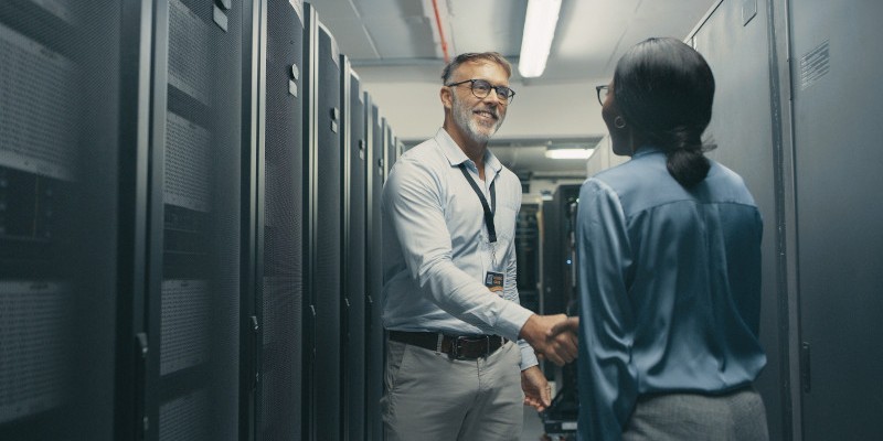 A man and woman shaking hands in a server room.