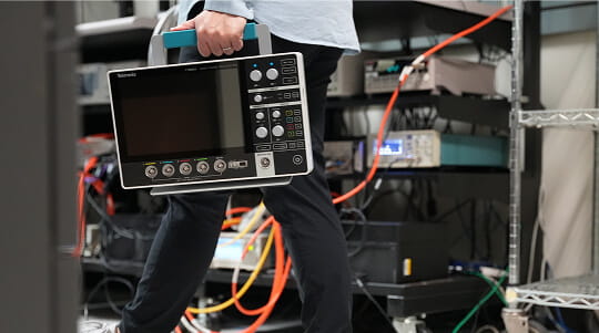 An engineer walking through a lab carrying a 2 Series Portable MSO Oscilloscope by the handle.